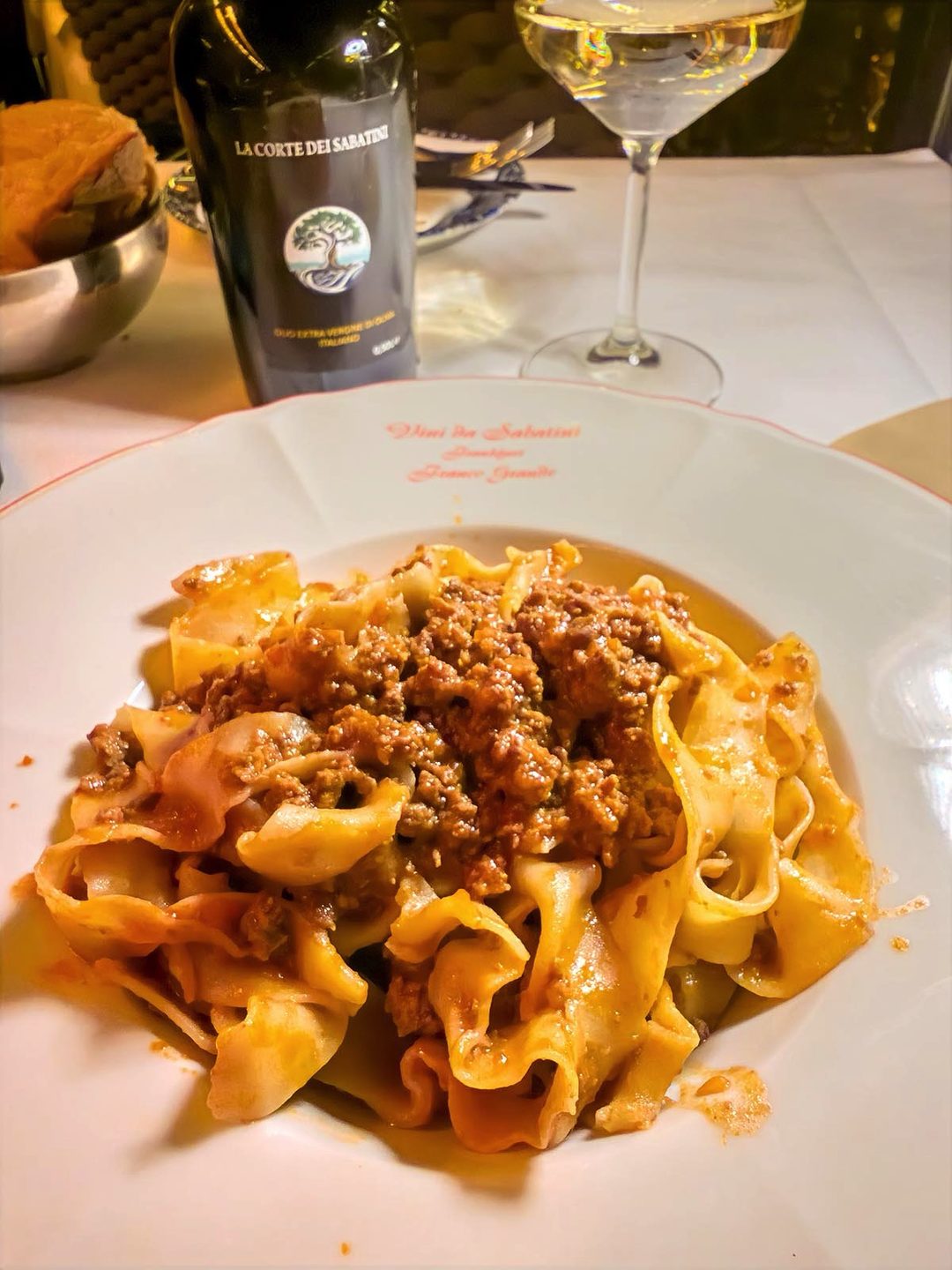 Hausgemachte Pappardelle mit Ragù, daneben ein Glas Weißwein