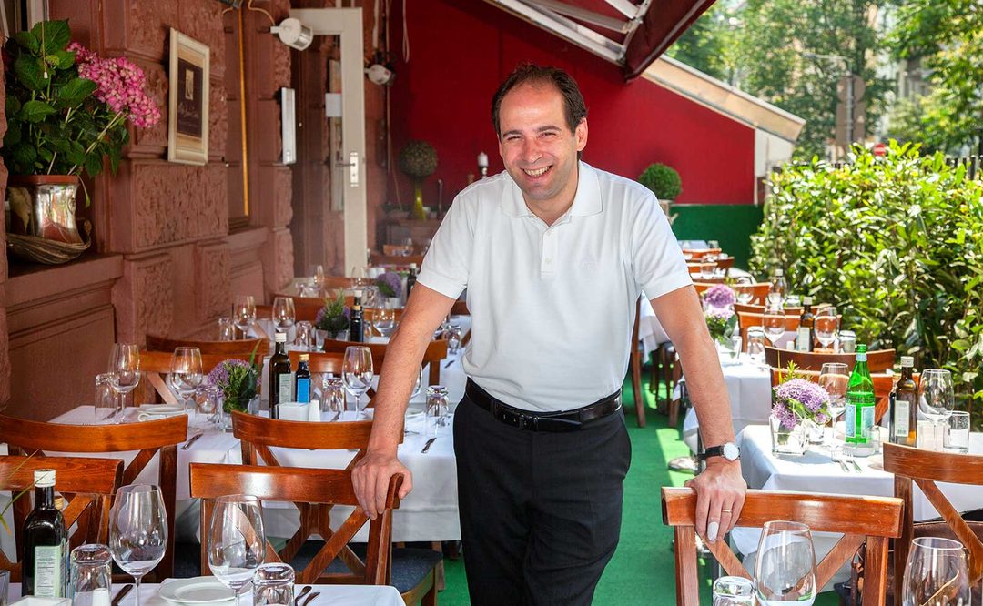 Franco Grande auf der begrünten Terrasse zwischen gedeckten Tischen